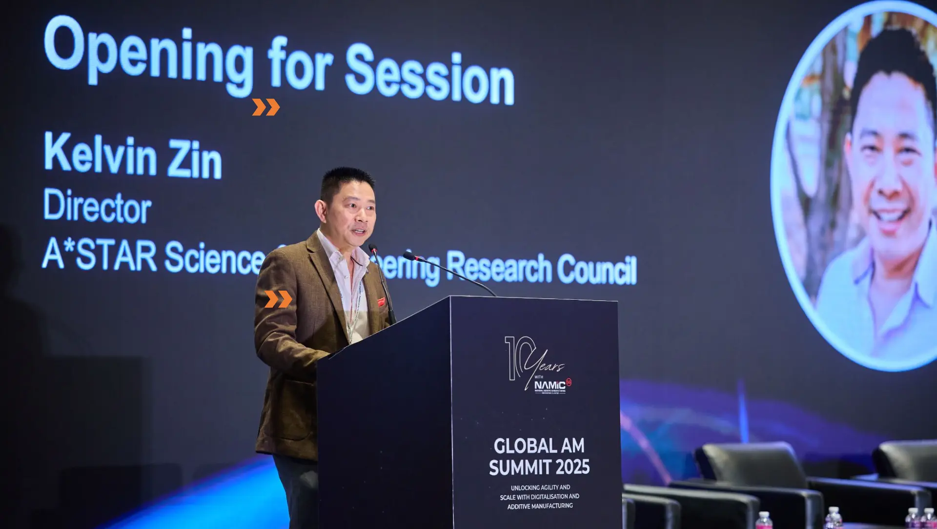 Keynote speaker at a branded lectern with presentation graphics on the main screen