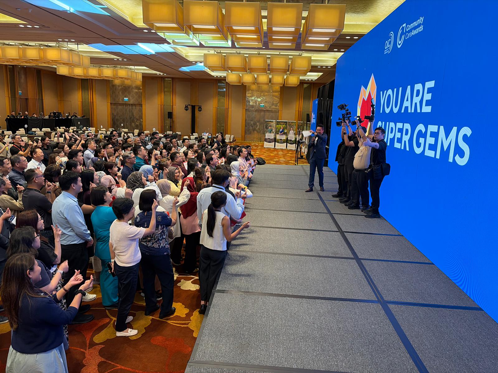 Large group of delegates posing in front of an LED wall during a community care awards segment
