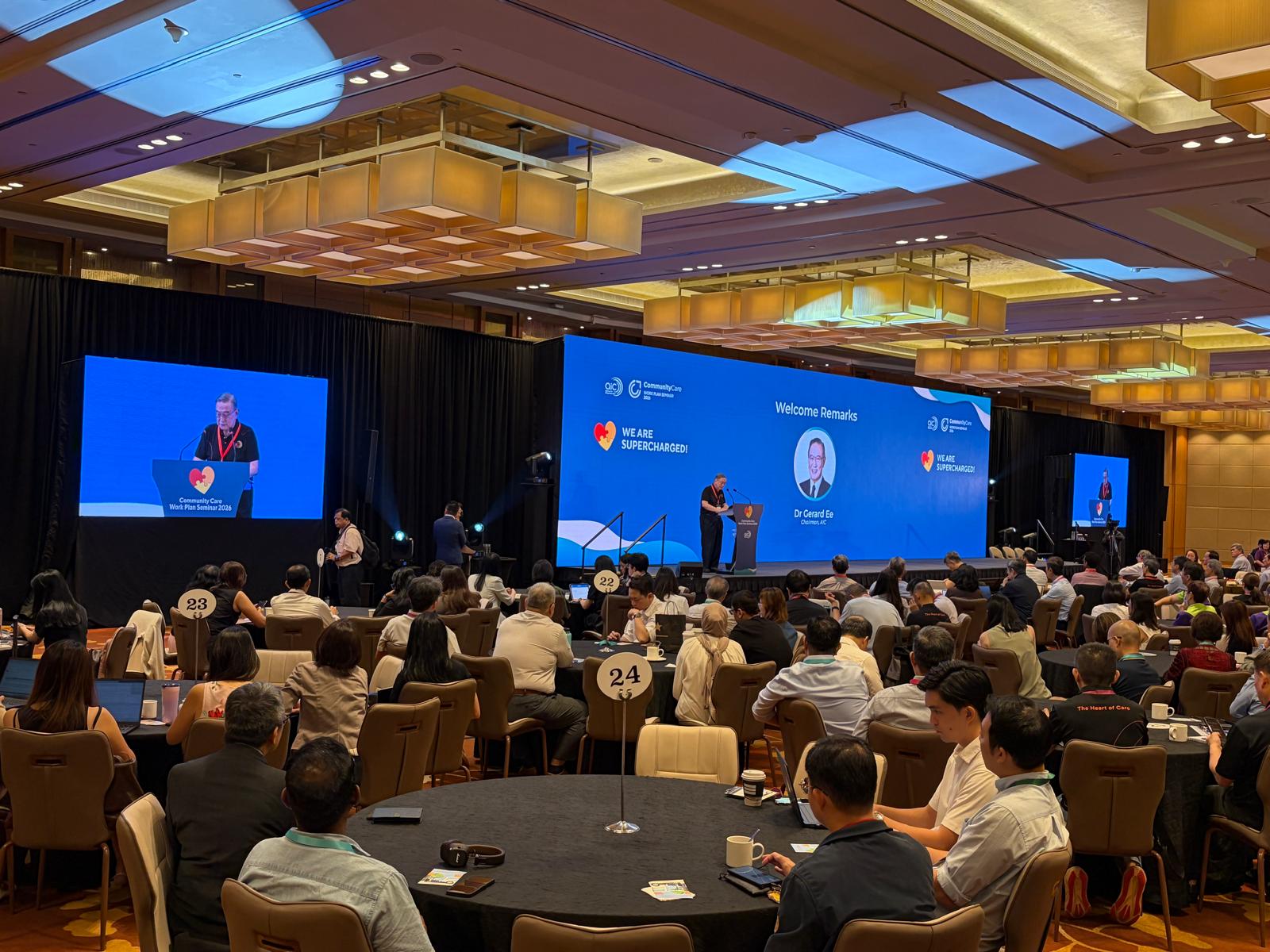 Wide ballroom plenary with dual LED screens during welcome remarks at a Singapore work plan seminar