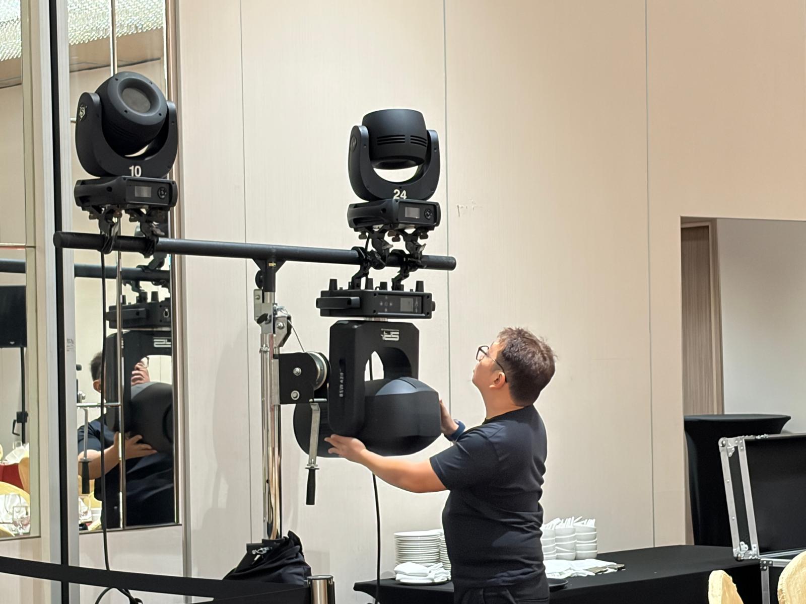 Technician rigging moving-head lighting fixtures on a lifting stand before an event