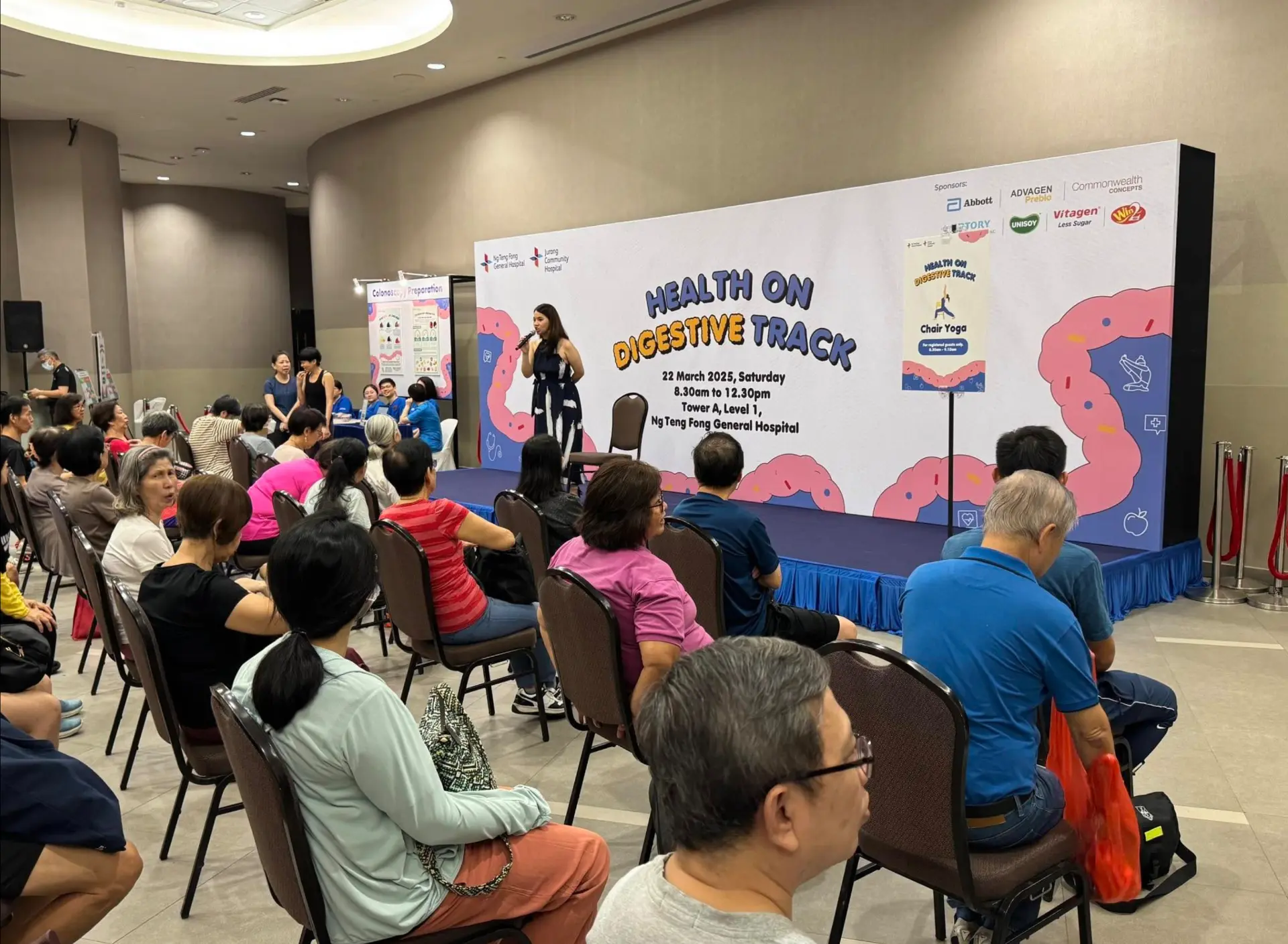 Speaker presenting on stage at a corporate health seminar with branded backdrop